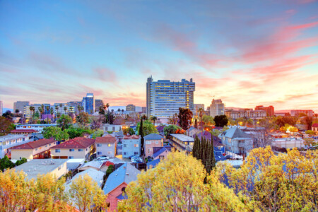 Foto: Impresionante vista de una ciudad al atardecer, con el Edificio Gouppers en el horizonte, rodeado de vibrantes colores y naturaleza urbana. Perfecto para reflejar innovación y energía positiva.