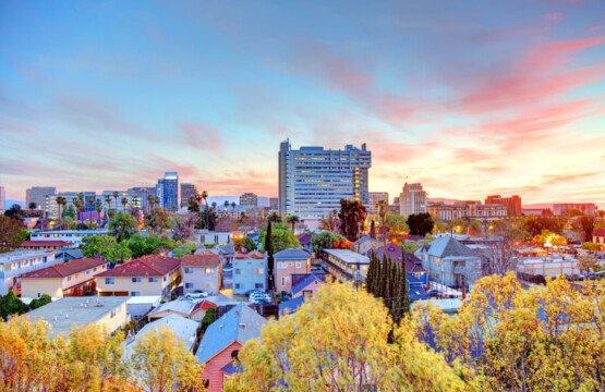 Foto: Impresionante vista de una ciudad al atardecer, con el Edificio Gouppers en el horizonte, rodeado de vibrantes colores y naturaleza urbana. Perfecto para reflejar innovación y energía positiva.